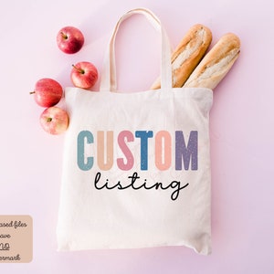 May include: A white tote bag with the text "CUSTOM listing" in colorful letters. The bag is on a pink background with apples and baguettes.