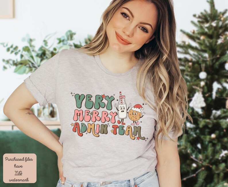 May include: A gray t-shirt with a Christmas-themed design featuring the text "Very Merry Admin Team" in a retro font. The design includes a cartoon milk carton and a cookie with a Santa hat.