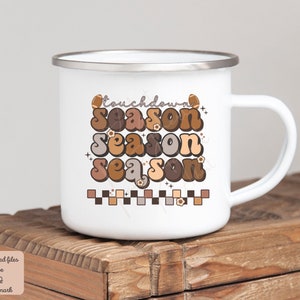 May include: White enamel mug with a brown, orange, and beige graphic that says "Touchdown Season" in a retro font. The graphic also includes footballs and small flowers.