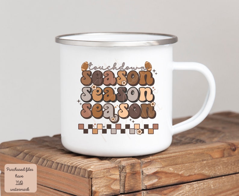 May include: White enamel mug with a brown, orange, and beige graphic that says "Touchdown Season" in a retro font. The graphic also includes footballs and small flowers.