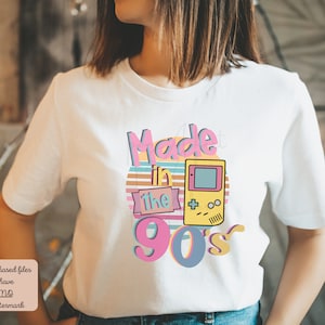 May include: White t-shirt with a graphic design that says "Made in the 90's" with a retro video game console graphic.