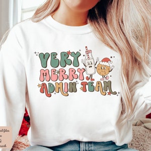 May include: White sweatshirt with a Christmas-themed graphic that says "Very Merry Admin Team". The graphic features a cartoon milk carton and a cookie with Santa hats.