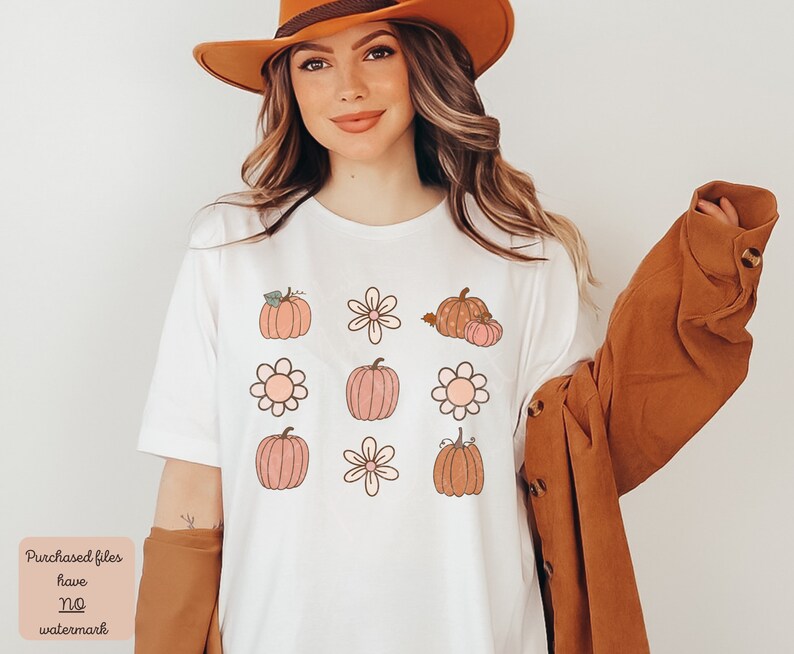 Op de afbeelding: Een wit T-shirt met een grafisch ontwerp van pompoenen en bloemen in tinten oranje, roze en bruin. Het ontwerp wordt negen keer op het shirt herhaald.