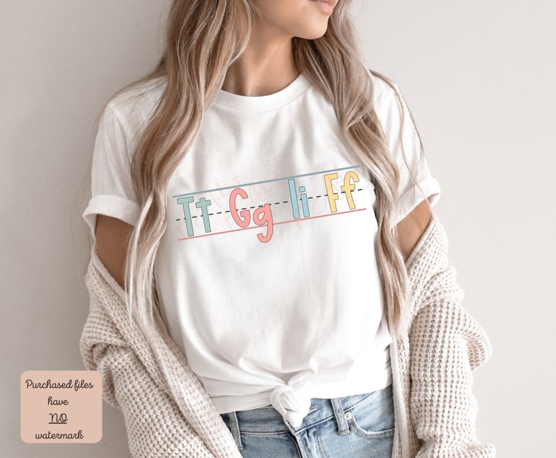 Pu&ograve; includere: Maglietta bianca con una grafica delle lettere "Tt Gg Li Ff" scritte in uno stile calligrafico colorato su uno sfondo a righe.