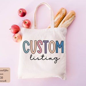 May include: A white tote bag with the text "CUSTOM listing" in colorful letters. The bag is on a pink background with apples and baguettes.