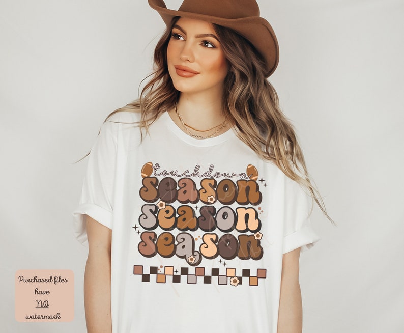 May include: White t-shirt with a brown, orange, and beige graphic that says "touchdown season season season". The graphic includes footballs and flowers.