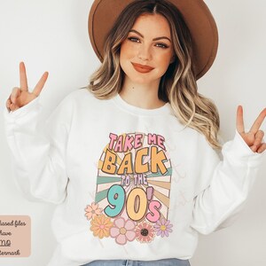 May include: White sweatshirt with a colorful graphic design that says "Take Me Back To The 90's". The graphic features a retro sunburst design with flowers.