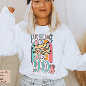 May include: White sweatshirt with a retro-style graphic design featuring a cassette tape and the text "Take Me Back to the 90s". The graphic is in shades of pink, blue, yellow, and green.