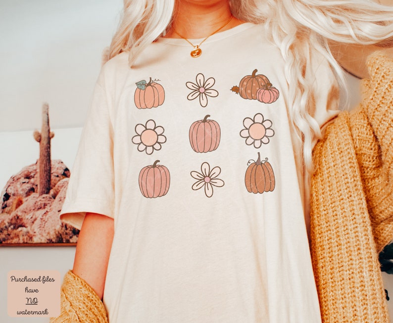 Op de afbeelding: Een wit T-shirt met een patroon van roze en bruine pompoenen en bloemen. De pompoenen hebben stelen en bladeren. De bloemen hebben vijf bloemblaadjes.