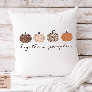 May include: White throw pillow with a graphic of three pumpkins. The pumpkins are orange, beige, and brown with a leopard print. The text "hey there, pumpkin" is printed below the pumpkins.