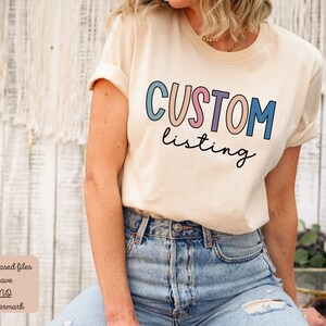 May include: A white t-shirt with the text "CUSTOM listing" in colorful letters. The letters are outlined in black and have a slight shadow effect. The text is centered on the shirt.