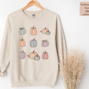 May include: A beige sweatshirt with a graphic of nine pastel colored pumpkins. The pumpkins are arranged in three rows of three.