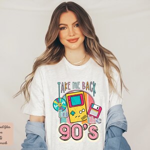 K&ouml;nnte beinhalten: Wei&szlig;es T-Shirt mit einem Grafikdesign, das ein Retro-Videospiel, eine Diskette und eine CD zeigt. Der Text auf dem Shirt lautet "Take Me Back to the 90's".
