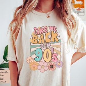 May include: A white t-shirt with a retro-style graphic that says "Take Me Back to the 90's" in colorful letters with a sunburst design and flowers.