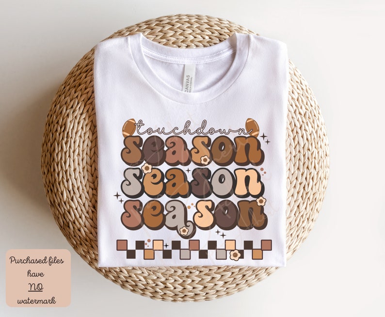 May include: White t-shirt with a brown, orange, and beige graphic design that says "touchdown season" with a football and flowers.