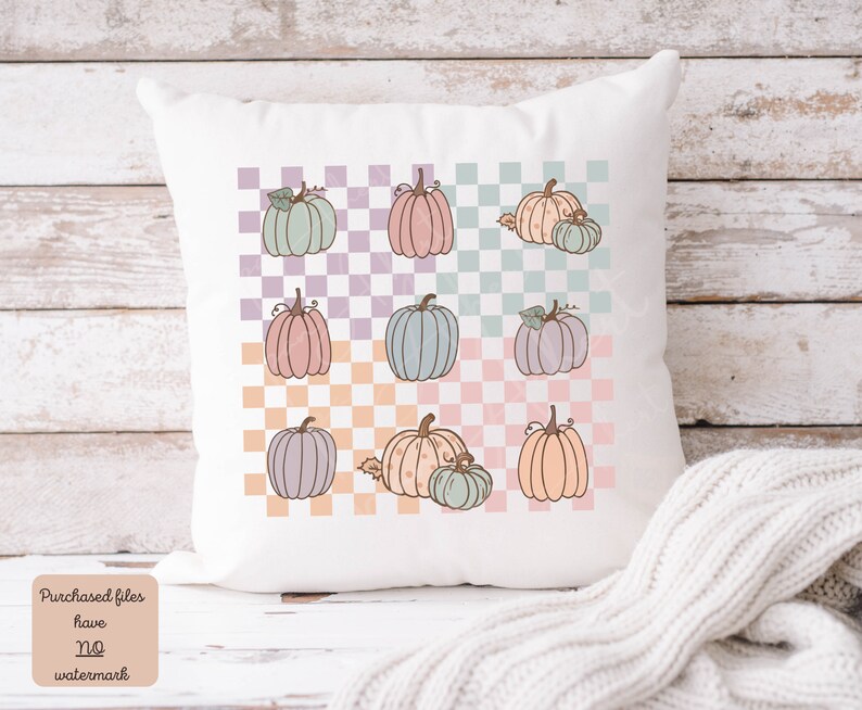 May include: A white cushion with a checkered pattern in pastel colours. The pattern features a repeating design of pumpkins in various shades of pink, blue, and orange.