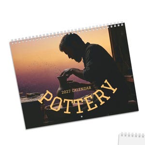 May include: A 2027 wall calendar featuring a silhouette of a person shaping a clay vessel on a pottery wheel at sunset. The cover displays the text POTTERY 2027 CALENDAR in bold, light-colored lettering against a warm orange and purple sky.