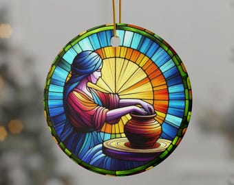 Può includere: Ornamento rotondo in ceramica con un'illustrazione in stile vetrata di una persona che lavora a un tornio da vasaio. L'ornamento ha un cordino dorato per appenderlo. L'opera d'arte utilizza una vivace tavolozza di blu, arancioni, rossi e gialli.