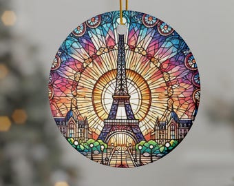 May include: Circular Christmas ornament with a stained-glass depiction of the Eiffel Tower in Paris. The ornament has a gold hanging string. The artwork features blue, orange, pink, and yellow hues.