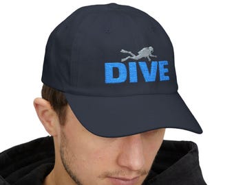 May include: Navy blue baseball cap with the word "DIVE" embroidered in blue block letters. A silver embroidered scuba diver is above the word "DIVE". The cap has a curved brim and a fabric strap closure.