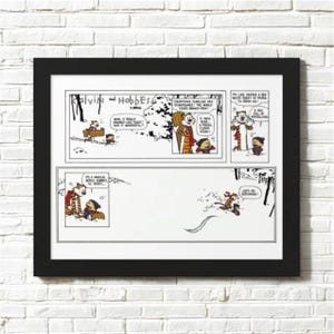 May include: A framed black and white comic strip featuring Calvin and Hobbes. The comic strip is divided into panels with speech bubbles. The frame is rectangular and hangs on a white brick wall.