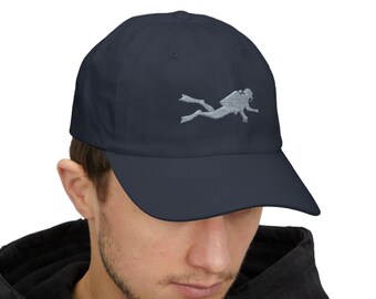 May include: Navy blue baseball cap with a silver embroidered scuba diver design. The cap has a curved brim and an adjustable strap for a comfortable fit. A stylish accessory for diving enthusiasts.