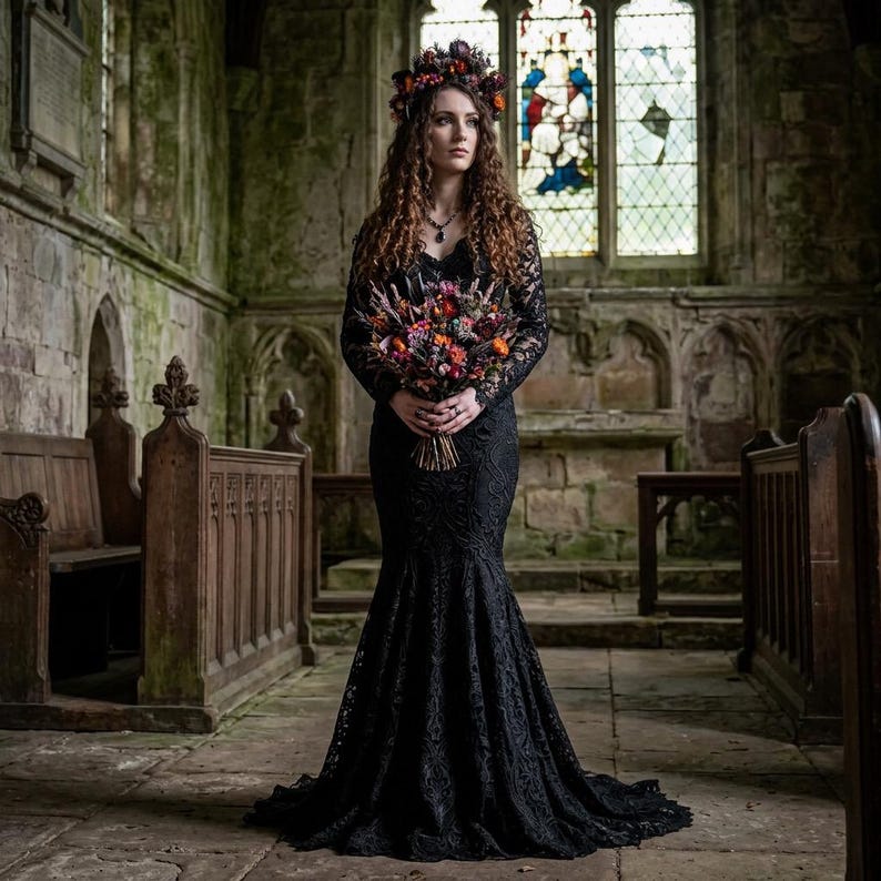 May include: A floor-length black lace gown with long sleeves and a fitted bodice that flares at the hem. The garment is paired with a floral crown and a large, colorful bouquet featuring orange, red, and purple flowers held at the waist.