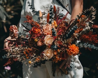Op de afbeelding: Een boeket gedroogde bloemen in tinten oranje, bruin en crème. Het boeket bevat rozen, eucalyptus en ander gedroogd gebladerte.