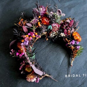 May include: A floral crown or bridal tiara composed of dried flowers in deep shades of purple, burgundy, orange, and pink, accented with dark foliage and thin stems. The text "BRIDAL TIARA" is printed in white in the bottom right corner.