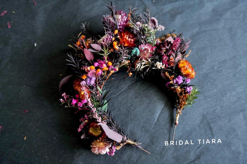 May include: A floral crown or bridal tiara composed of dried flowers in deep shades of purple, burgundy, orange, and pink, accented with dark foliage and thin stems. The text "BRIDAL TIARA" is printed in white in the bottom right corner.