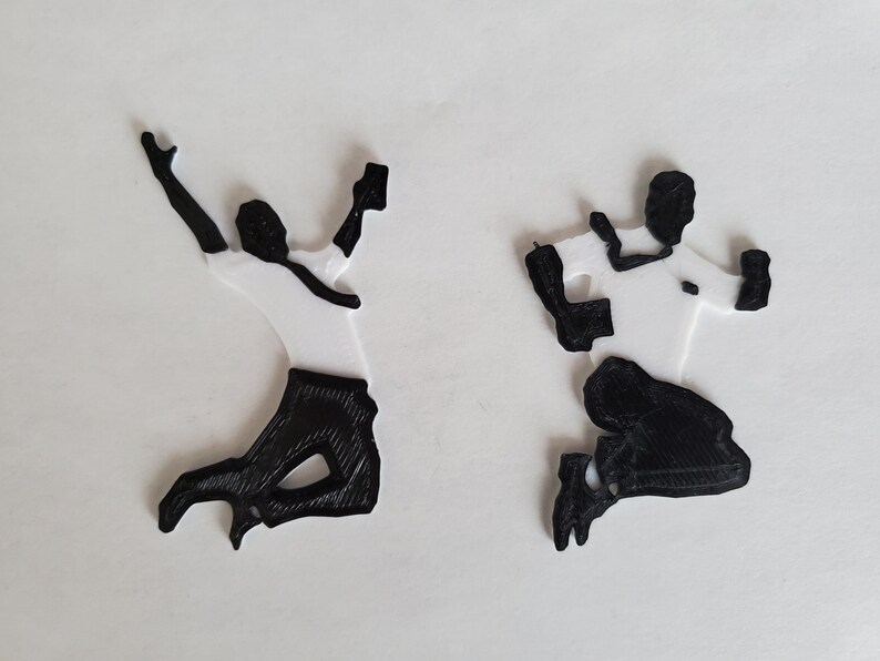 Op de afbeelding: Twee zwart-witte 3D-geprinte figuren van mensen die in de lucht springen.