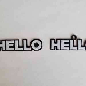 Op de afbeelding: Twee zwarte plastic borden met de tekst "HELLO" in witte letters. Een bord heeft een kleine lus aan de bovenkant.