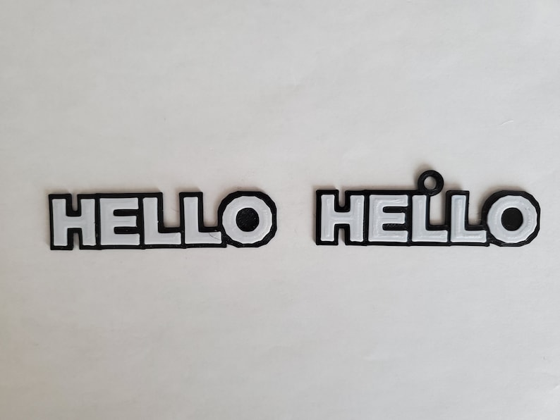 Op de afbeelding: Twee zwarte plastic borden met de tekst "HELLO" in witte letters. Een bord heeft een kleine lus aan de bovenkant.