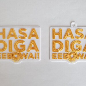 Op de afbeelding: Twee witte rechthoekige ornamenten met de woorden "HASA DIGA EEBO WAI!" in gouden letters.