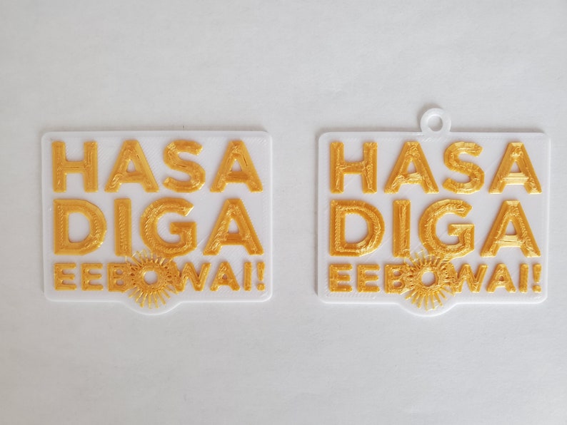 Op de afbeelding: Twee witte rechthoekige ornamenten met de woorden "HASA DIGA EEBO WAI!" in gouden letters.