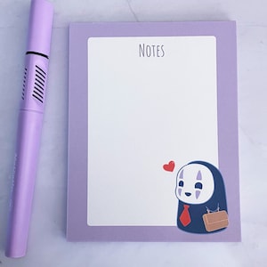 May include: A purple notepad with a white interior and a purple border. The notepad has the word "NOTES" printed at the top. A cartoon illustration of a character from the movie Spirited Away is at the bottom of the notepad.