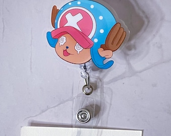 Puede incluir: Un personaje de dibujos animados azul y rosa con una cruz blanca en un sombrero rosa. El personaje está unido a un soporte de credencial retráctil de plástico transparente.