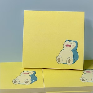 May include: A stack of yellow sticky notes with a cartoon illustration of a blue and white Pokemon character on the top note.
