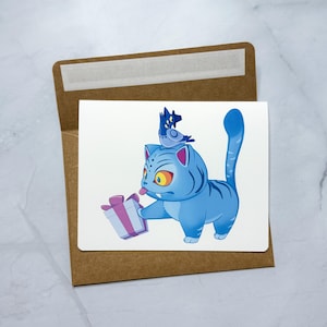 May include: A greeting card featuring a blue cartoon cat holding a gift box with a purple bow. The cat has yellow eyes and a small blue bird on its head. The card is inside a brown envelope.