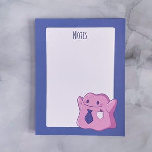 May include: A blue notepad with a white border and the word "NOTES" printed at the top. A pink cartoon ghost with a blue tie and a pocket is at the bottom of the notepad.