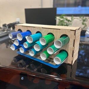 May include: A wooden organizer with 10 slots for storing rolls of vinyl. The rolls are in shades of blue and green.