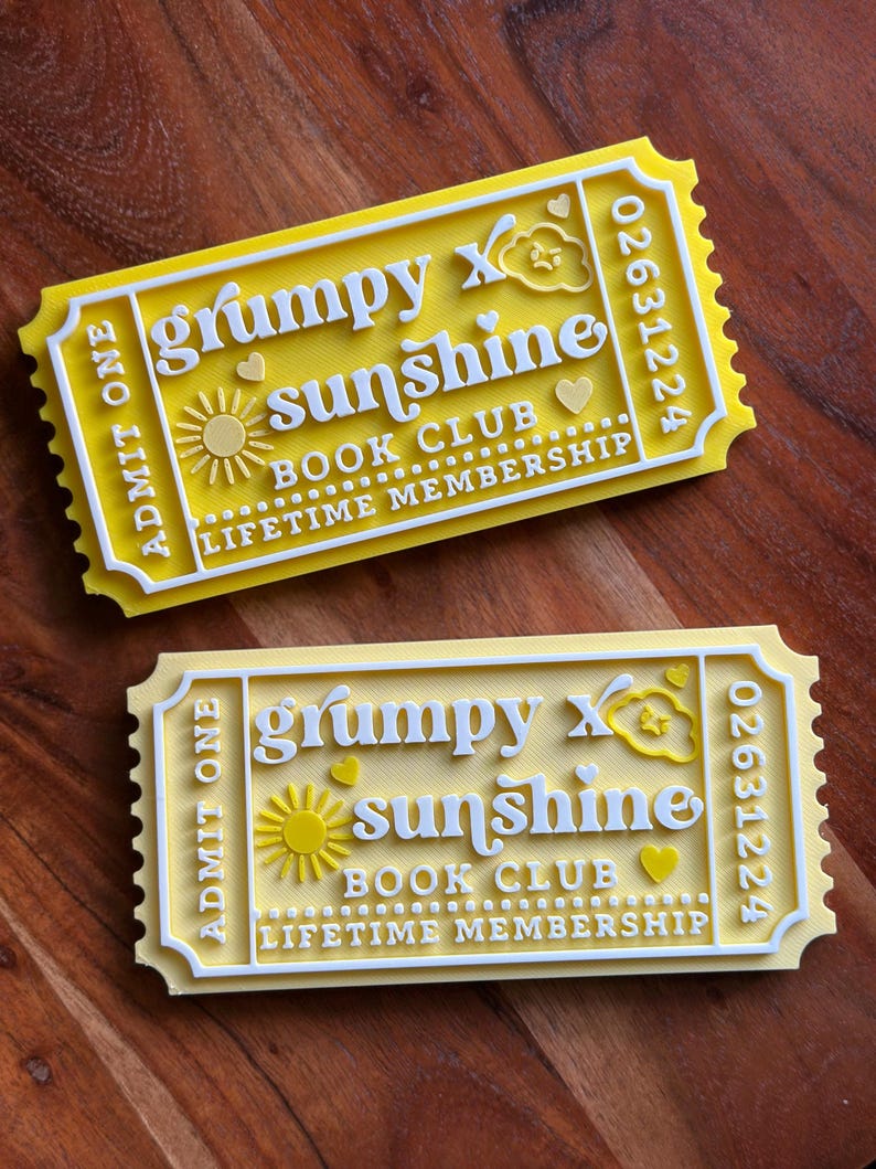Puede incluir: Dos boletos amarillos y blancos con el texto "grumpy x sunshine BOOK CLUB LIFETIME MEMBERSHIP". Los boletos tienen un dise&ntilde;o de sol, nube y coraz&oacute;n. Los boletos son rectangulares con un borde festoneado y las palabras "ADMIT ONE" a la izquierda.