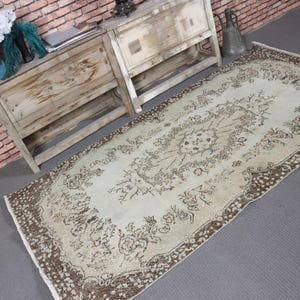 May include: A cream-coloured, rectangular rug with a detailed brown border and intricate floral patterns. The central field of the rug is cream, with the brown border and patterns adding a vintage aesthetic. The rug is likely made of woven material and would suit a living space.