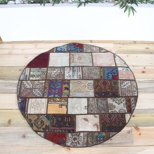 Könnte beinhalten: Ein runder Teppich mit einem Patchwork-Design, das aus verschiedenen rechteckigen Stoffsegmenten besteht. Der Teppich zeigt eine vielfältige Farbpalette mit Tönen in Dunkelrot, Blau, Braun, Creme und Beige sowie komplizierten Webmustern.