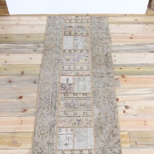 May include: A rectangular patchwork runner rug featuring a central column of varied rectangular textile segments in muted tones of beige, gray, and soft lavender, flanked by two wider side panels with intricate, faded floral and geometric patterns.