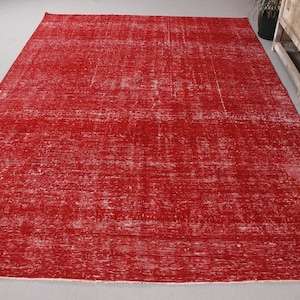May include: A large, rectangular red rug with a distressed, vintage appearance. The rug's color is a vibrant red with lighter, faded areas, creating a textured effect. The rug is likely made of woven material and is suitable for a living room or bedroom.