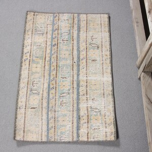 May include: A rectangular area rug featuring a faded, distressed pattern in shades of beige, light blue, and brown. The design consists of vertical bands with intricate, worn geometric motifs and a thin, dark-colored border around the edges.