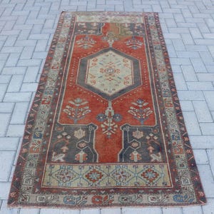 May include: A rectangular area rug featuring a central hexagonal medallion in cream and dark gray, set against a vibrant orange field. The rug displays intricate floral motifs, geometric borders, and a palette of muted blue, red, and tan accents.
