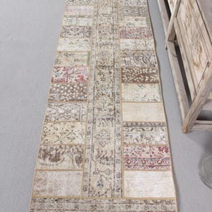 Op de afbeelding: Een lange, rechthoekige vloerkleed met een patchwork-ontwerp. Het vloerkleed heeft verschillende rechthoekige patches in tinten beige, bruin, rood en groen. Het vloerkleed is waarschijnlijk gemaakt van geweven stof en is geschikt voor een hal of entree.