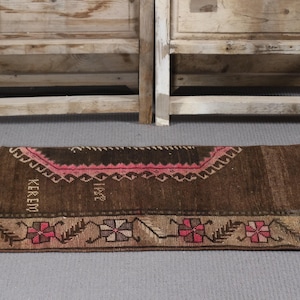 Peut inclure: Un tapis brun et rose à motifs avec le mot "KEREM" et le nombre "1942" tissés dans le motif.